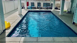 Une piscine rectangulaire à l’eau d’un bleu limpide, entourée d’un patio couvert agrémenté de chaises et de tables.