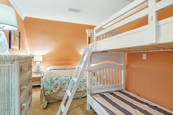 Habitación con literas, pared naranja, cabecero blanco y colchón a rayas.
