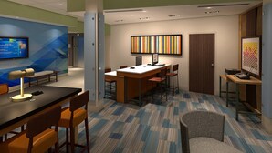 Een moderne hotelkamer met een bureau, stoelen, een computer en een flatscreen televisie.