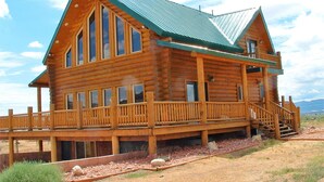 A log cabin with a metal roof, large windows, and a wooden deck. - Red Rock Ranch Log Cabin: Large, Fully Furnished, 5 Bdr, sleeps 12, 3 levels (Escalante)