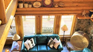 A cozy cabin interior with a green leather sofa, a wooden bench, and a stone fireplace. - Red Rock Ranch Log Cabin: Large, Fully Furnished, 5 Bdr, sleeps 12, 3 levels (Escalante)