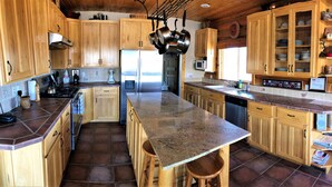 A kitchen with wooden cabinets, a granite countertop, stainless steel appliances, and a hanging pot rack. - Red Rock Ranch Log Cabin: Large, Fully Furnished, 5 Bdr, sleeps 12, 3 levels (Escalante)