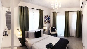 A hotel room with a bed, a chair, a desk, and a chandelier.