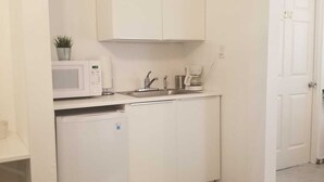 A compact kitchen with white cabinets, a microwave, a coffee maker, and a refrigerator.