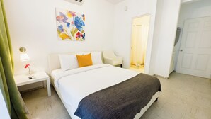 Una habitación de hotel con cama, mesita de noche, lámpara, un cuadro y una puerta.