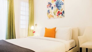 Habitación de hotel con cama, mesita de noche, lámpara, silla y un cuadro en la pared.