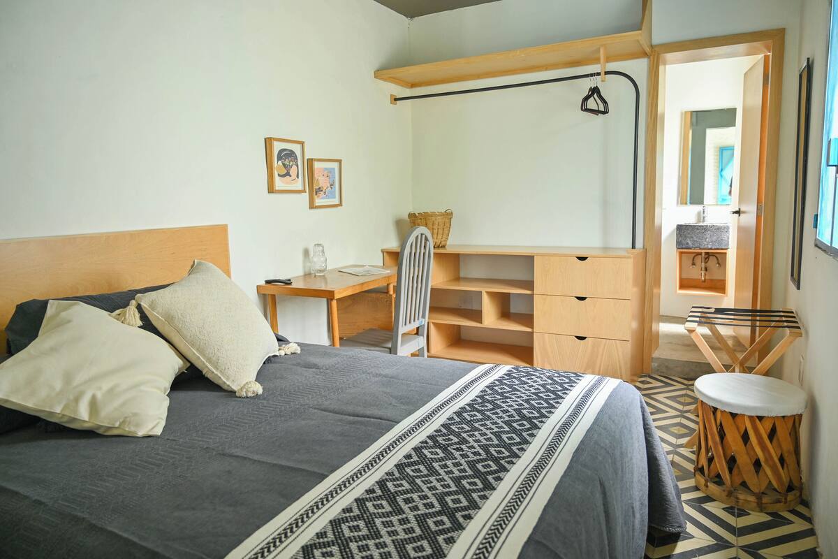 Een slaapkamer met een bed, nachtkastje en bureau met stoel. Uitslaapkast, spiegel en een klein krukje zijn aanwezig.