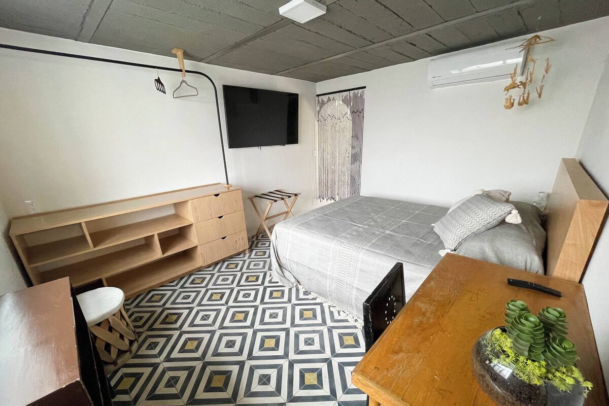 Een slaapkamer met een bed, een bureau, een stoel, een televisie en een kleine plant.