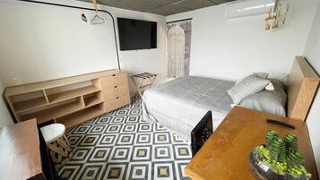 A bedroom with a bed, a desk, a chair, a TV, and a small plant.