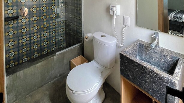Een badkamer met een betegelde douchewand, toilet, een houten medicijnkastje en een granieten wastafel.