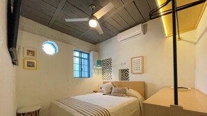 A bedroom with a bed, a ceiling fan, a window, and a wall-mounted air conditioner.