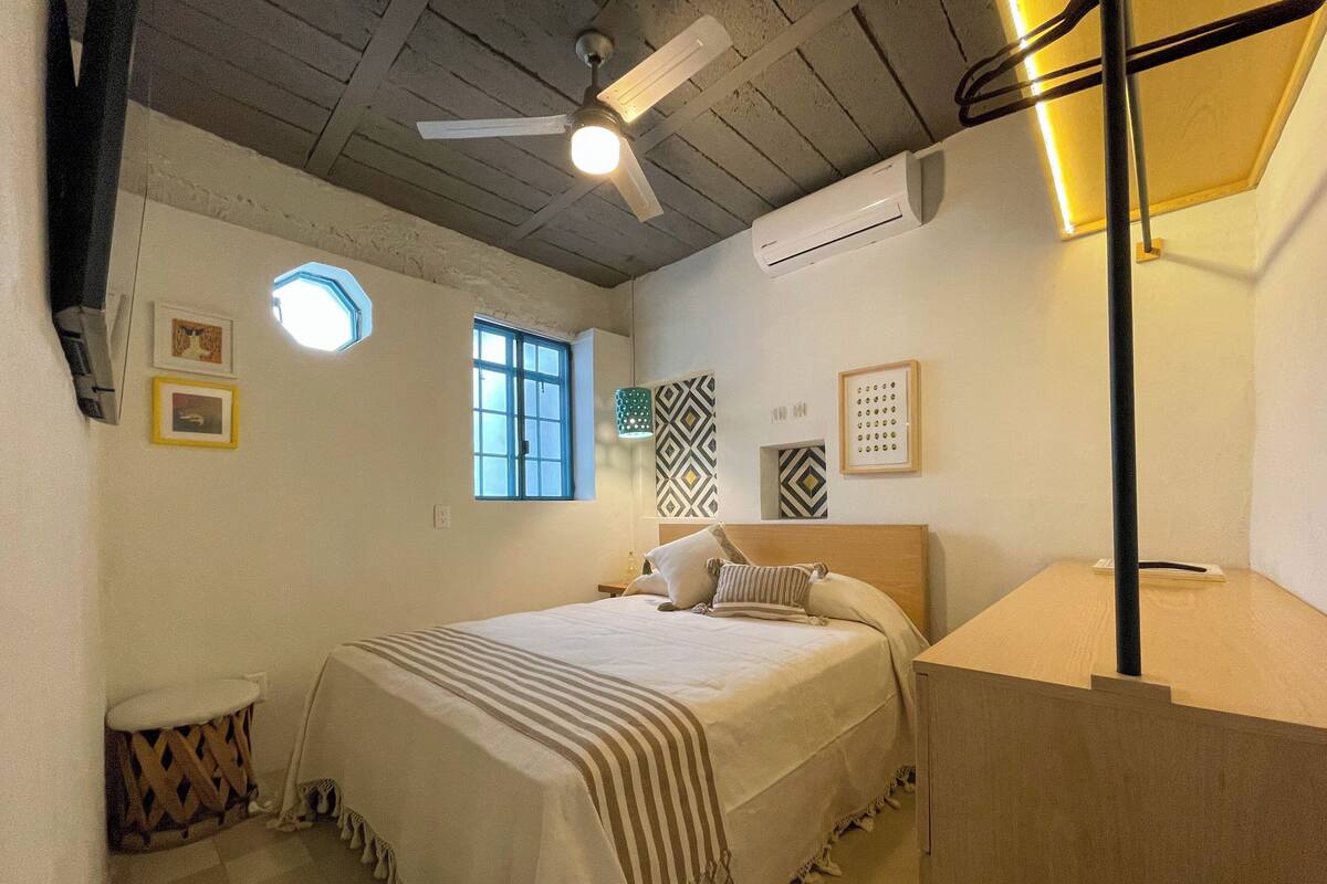 Een slaapkamer met een bed, een plafondventilator, een raam en een wandairconditioner.
