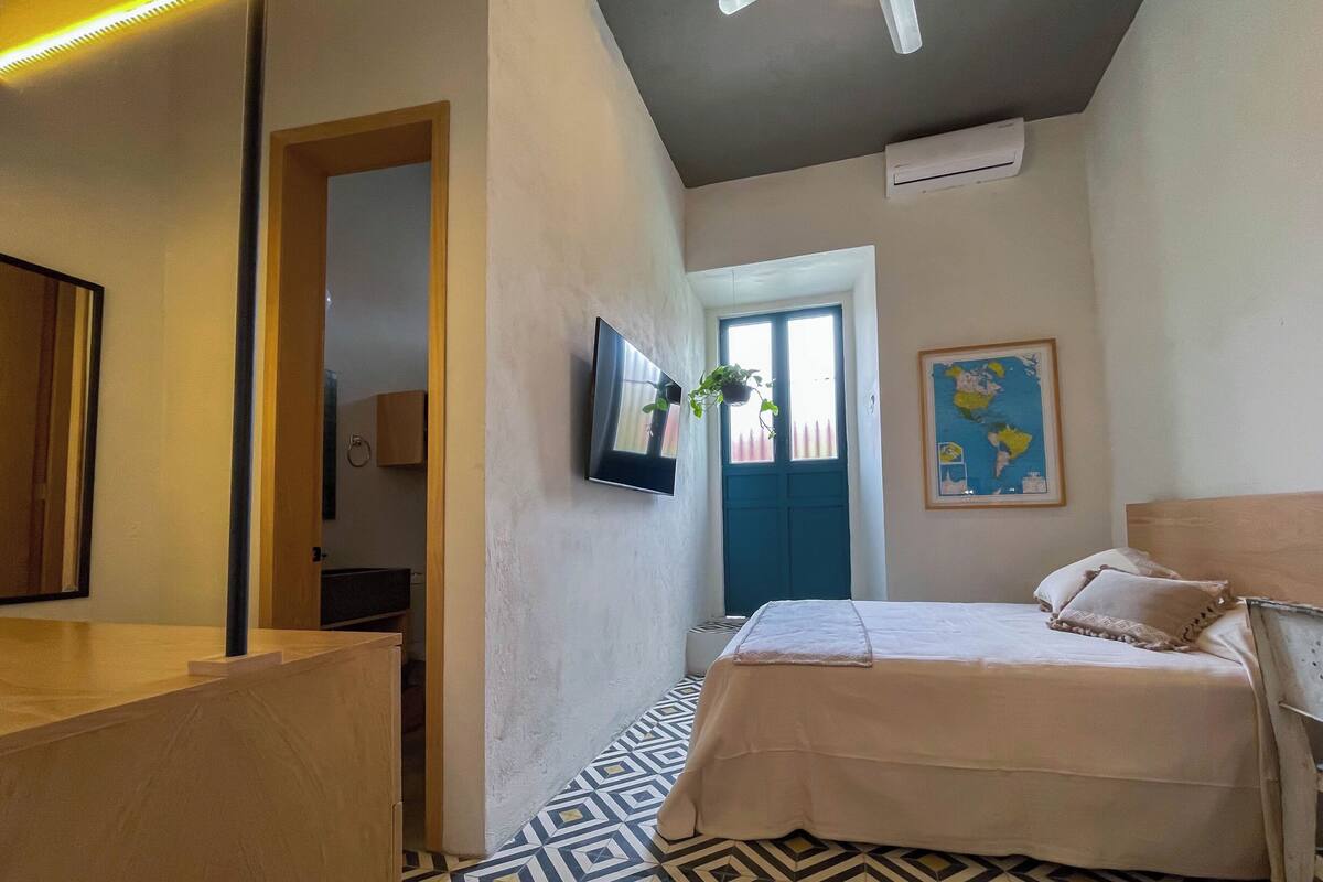 Een slaapkamer met een bed, een aan de muur bevestigde televisie, een kaart en een raam met uitzicht.
