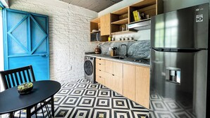 A compact kitchen with a washing machine, wooden cabinets, a stainless steel refrigerator, and a blue door.