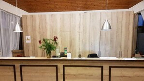 A reception desk with a wooden panel backdrop, two pendant lights, a vase with flowers, and a small statue. - Holzchalet A-D by Interhome (Gerolstein)