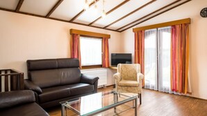 A modern living room with a leather sofa, a glass coffee table, a patterned armchair, and a television on a stand. - Holzchalet A-D by Interhome (Gerolstein)