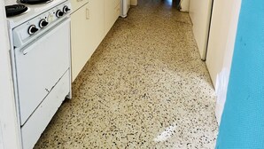 A narrow kitchen with white cabinets, a stove, a microwave, and a refrigerator. A dining area with a table and chairs is visible in the background. - Condo with King Size Bed, near Downtown, with Ocean Views, AC, and Secured. (Christiansted)