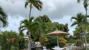 An outdoor patio with a round table and chairs, a large umbrella, and a barbecue grill. - Condo with King Size Bed, near Downtown, with Ocean Views, AC, and Secured. (Christiansted)