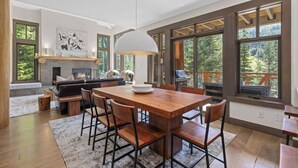 Eine moderne Küche mit einem Holztisch, Barhocker und einem großen Fenster mit Blick auf einen Wald.