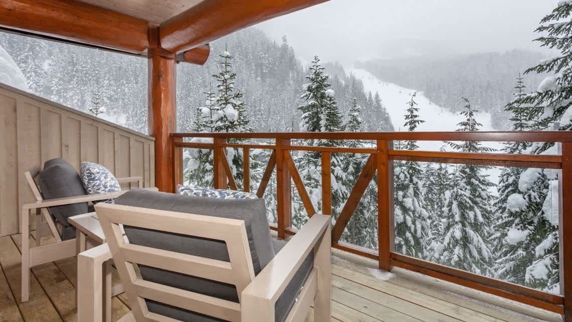 A wooden deck with a view of snow-covered trees and mountains.