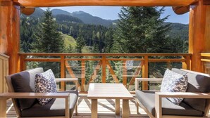 Eine Holzterrasse mit zwei Sofas und einem Tisch, mit Blick auf eine bewaldete Berglandschaft.