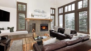 Ein modernes Wohnzimmer mit Kamin, Ledersofas und großen Fenstern mit Blick auf Bäume.