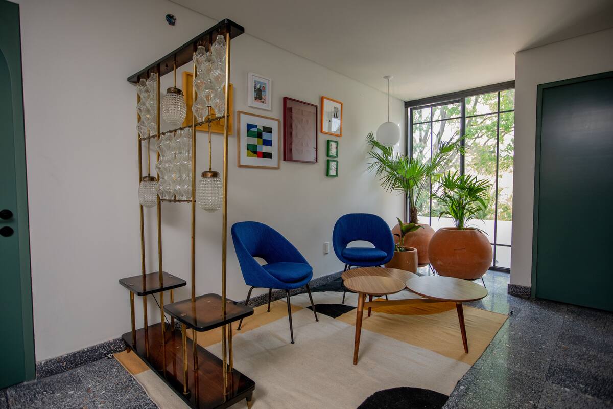 Un moderno vestíbulo con dos sillas azules, una mesa de centro de madera y una lámpara de cristal decorativa.