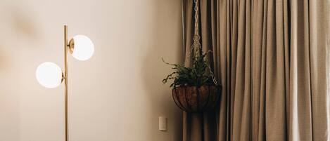 Ein Zimmer mit einem roten Sessel, einer Stehlampe, einer hängenden Pflanze, einem kleinen Hocker und einem gemusterten Teppich.