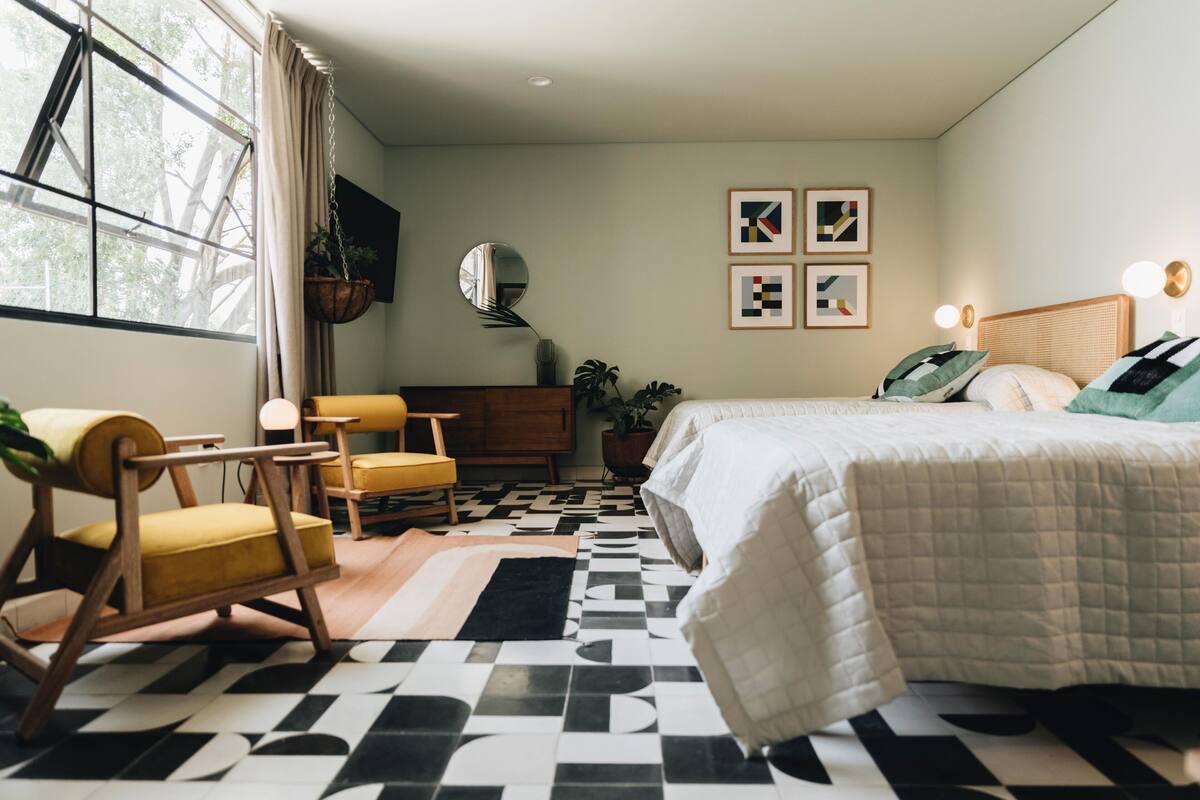Un dormitorio con cama, una silla, cómoda, espejo y cuadros en la pared.