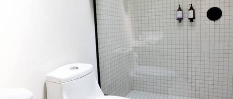 Ein modernes Badezimmer mit einer weißen Toilette, einer Dusche inklusive schwarzem Brauseschlauch und einem Fußboden mit Gittermuster.
