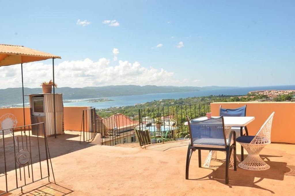 A terrace with a table and chairs, overlooking a coastal view with mountains in the distance.