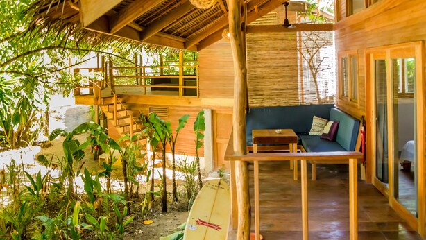 A wooden interior with a sofa and table, surrounded by plants and a surfboard. - Amihan Bungalows (Cloud Nine) (General Luna)