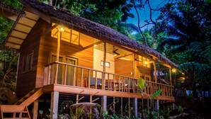 A wooden cabin with a thatched roof, surrounded by lush vegetation. - Amihan Bungalows (Cloud Nine) (General Luna)