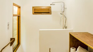 A bathroom with a window, a shower, a toilet, and a shelf with towels. - Amihan Bungalows (Cloud Nine) (General Luna)