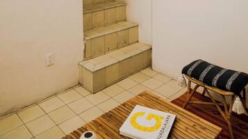 Una escalera que lleva a un piso superior, un cuadro enmarcado en la pared, un banco con cojín y un libro en el suelo.