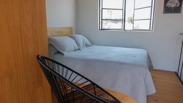 A bedroom with a bed, a window, a chair, and a wooden floor.