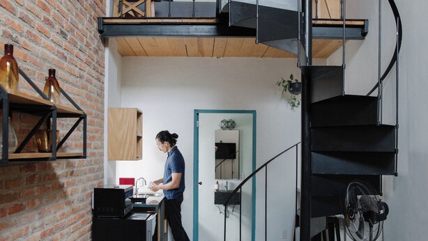 A modern kitchen with a brick wall, a wooden counter, and a black spiral staircase.