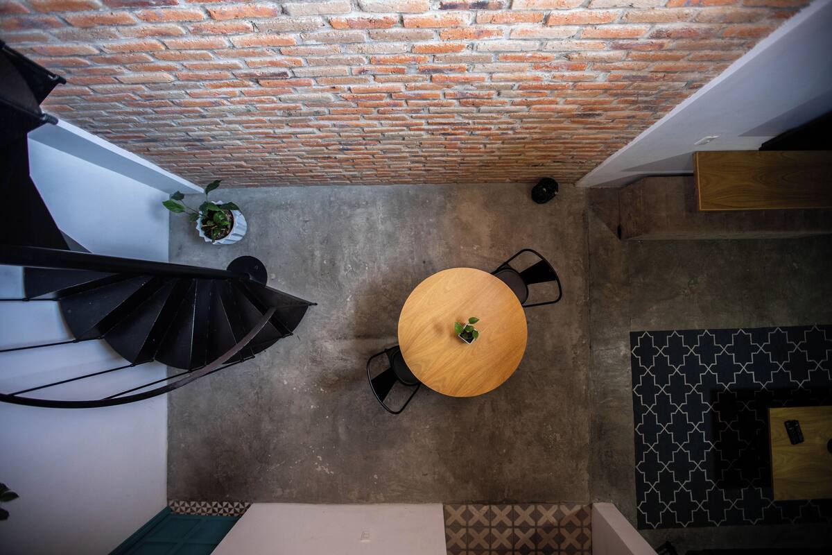 Une pièce avec un plafond en briques, une table ronde en bois entourée de chaises, une plante en pot et un mur orné d’un motif.