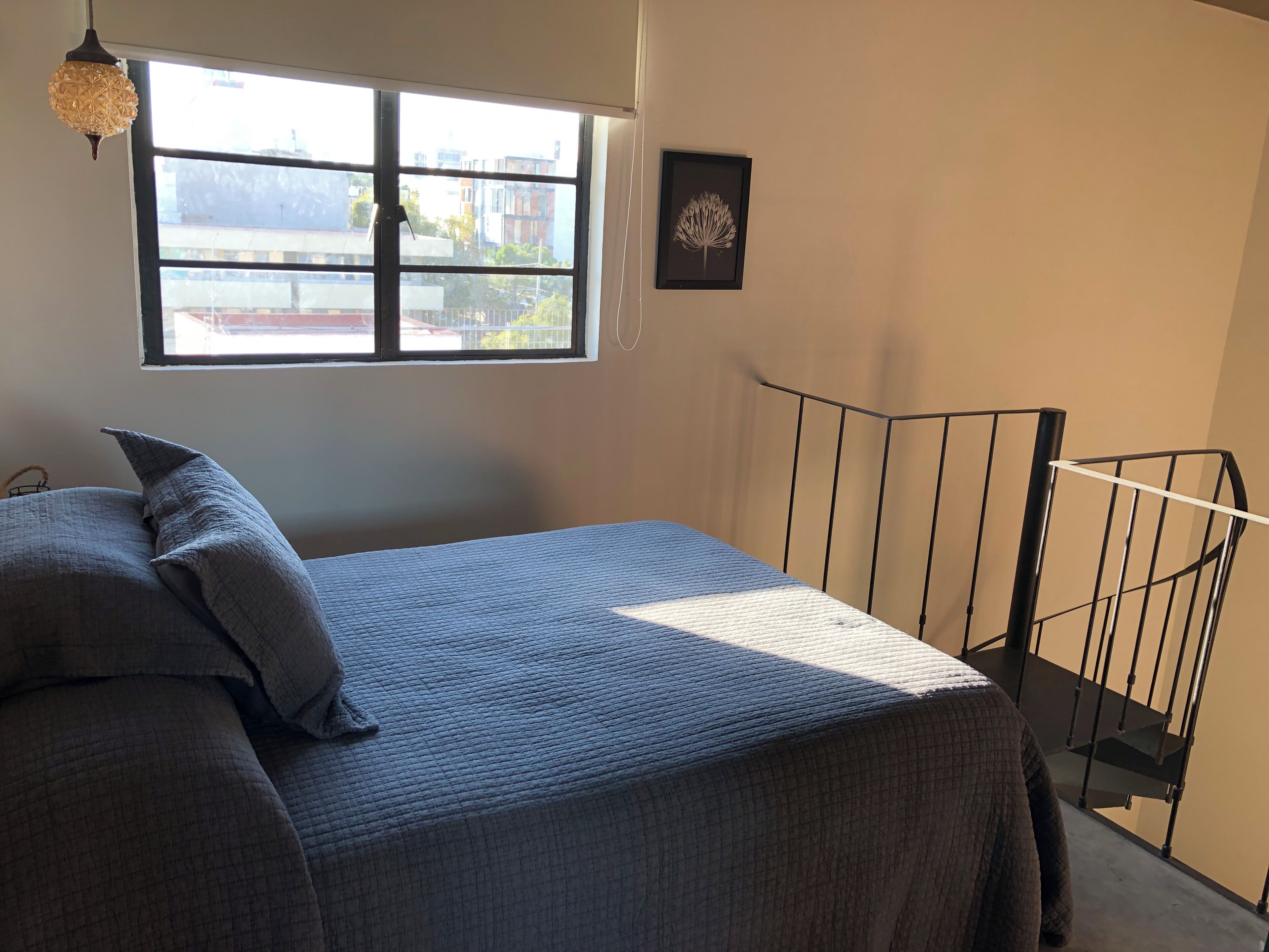 A bedroom with a bed, a window, a framed picture, and a staircase.