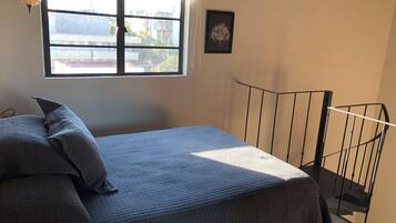 A bedroom with a bed, a window, a framed picture, and a staircase.