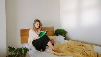 A person sitting on a bed with a wooden headboard, reading a book.