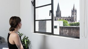 A room with a large window, a bed, a potted plant, and a view of a cathedral.