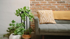 A grey sofa with a patterned throw blanket against a brick wall.
