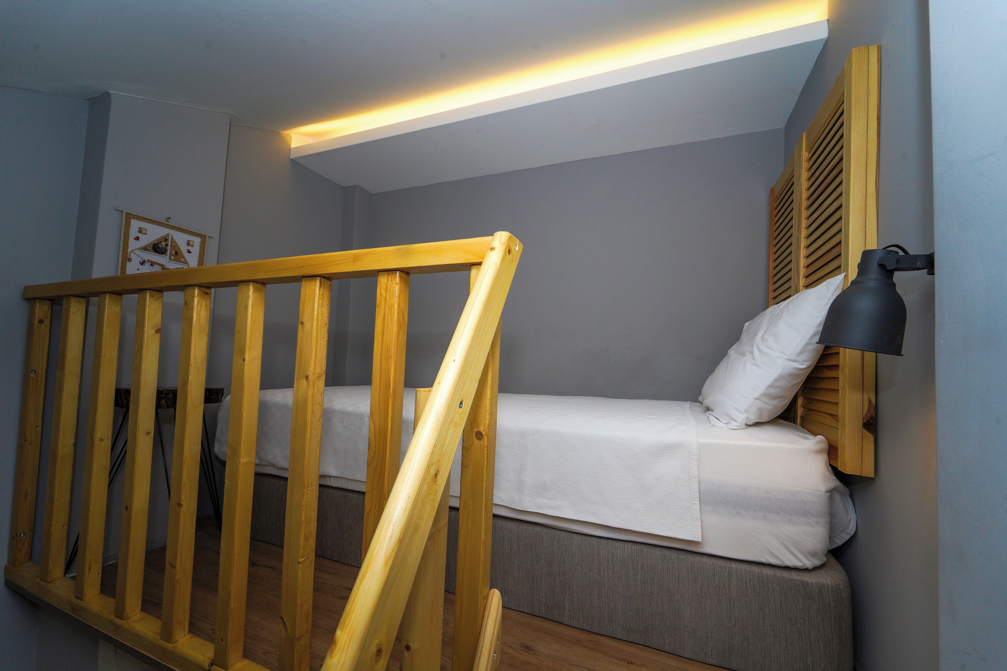 Una habitación pequeña y acogedora con una cama individual, baranda de madera y una lámpara de noche.