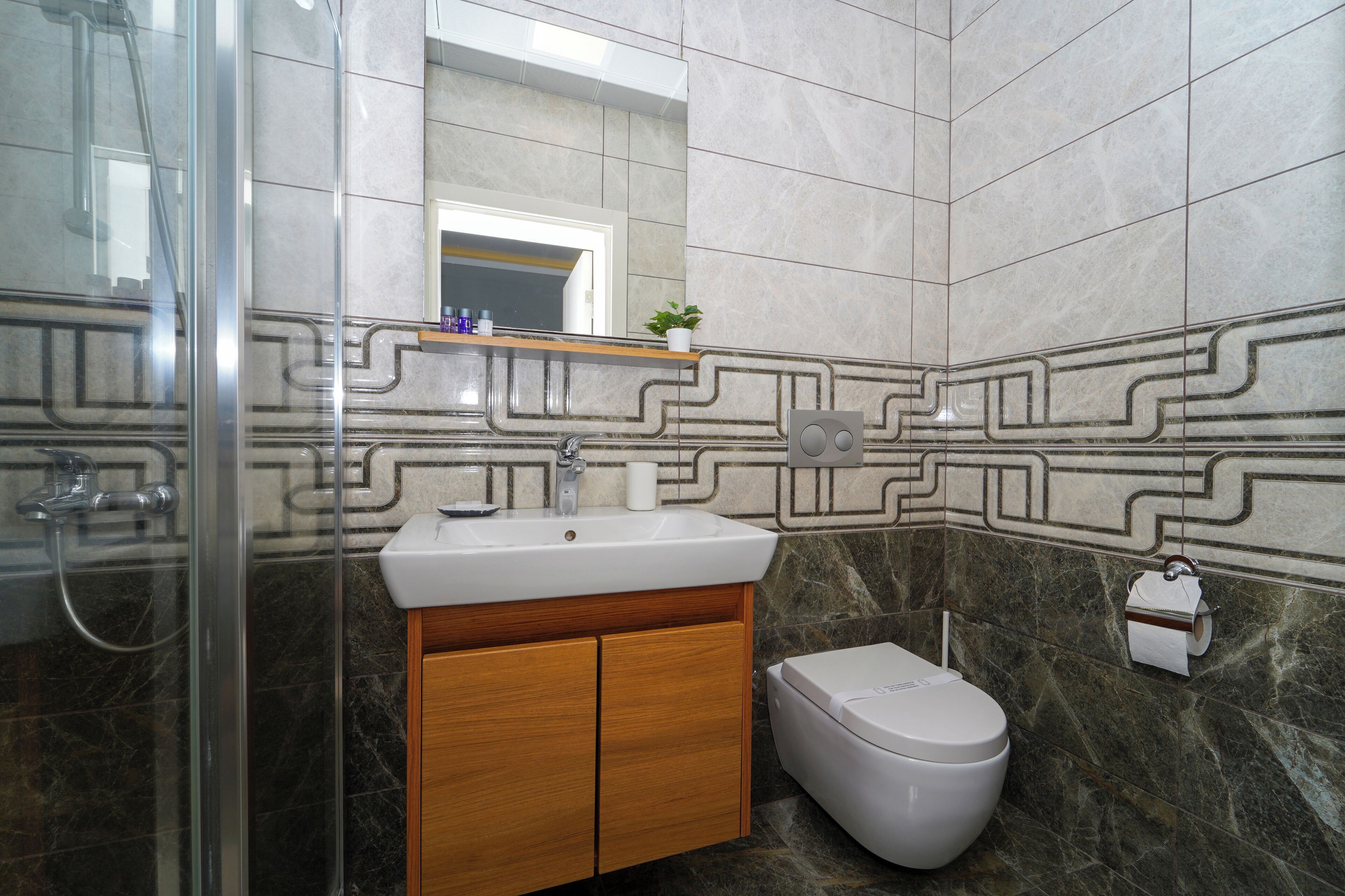 Un baño con cabina de ducha de vidrio, lavabo con mueble de madera, inodoro y azulejos decorativos.