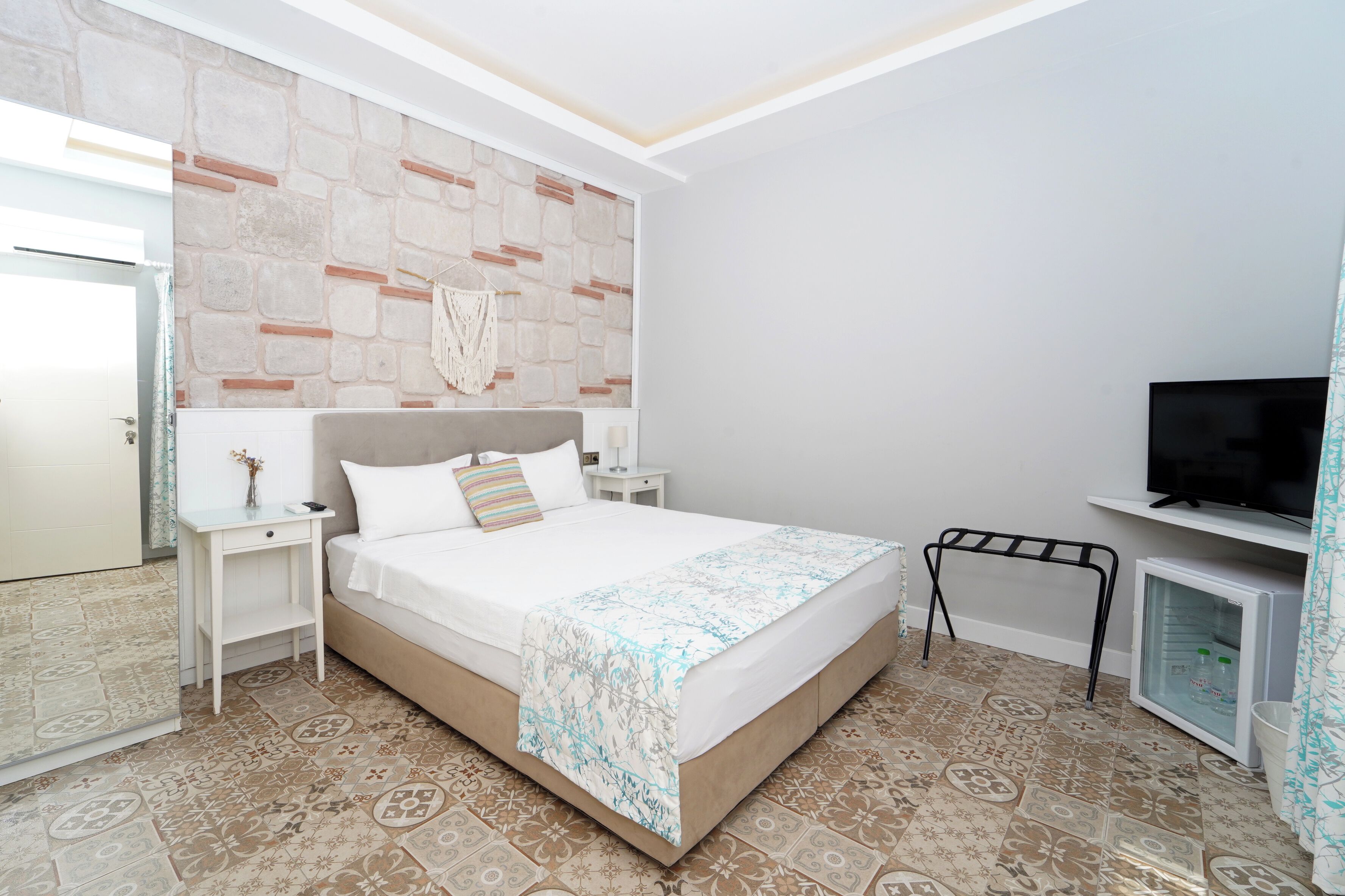 Un dormitorio con cama, televisor, un mueble pequeño y un detalle decorativo en la pared.