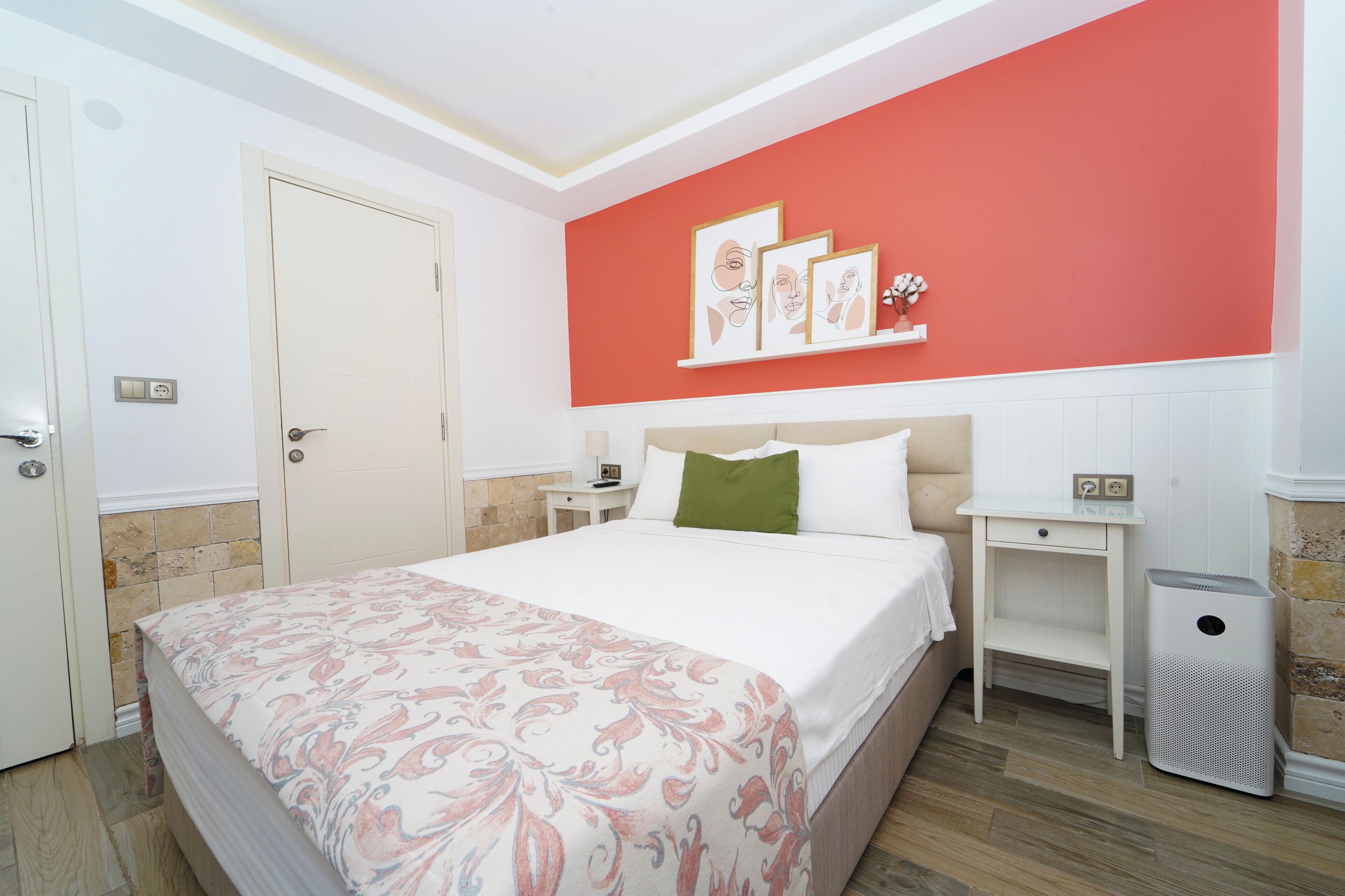 A neatly arranged bedroom with a bed, bedside tables, a red accent wall, and a white door.
