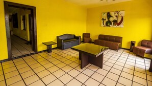 Quarto com paredes amarelas, um ventilador de teto, um sofá, uma mesa e um quadro.
