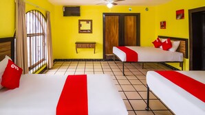 Quarto de hotel com duas camas, ventilador de teto, televisão e janela com cortinas.