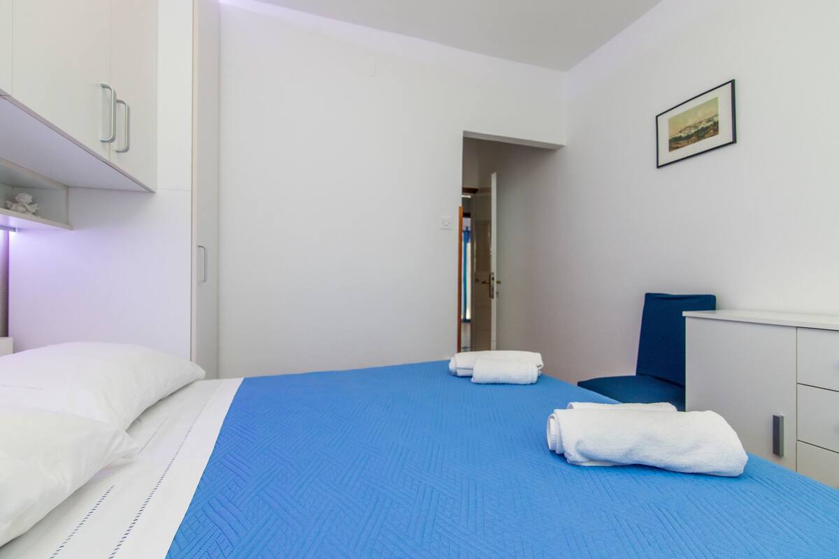 A hotel room with a bed, a chair, a desk, and a door leading to another room.